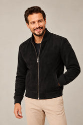 Male model wearing a black suede bomber jacket with a rib-knit collar, silver-tone front zipper, side pockets and ribbed trims.