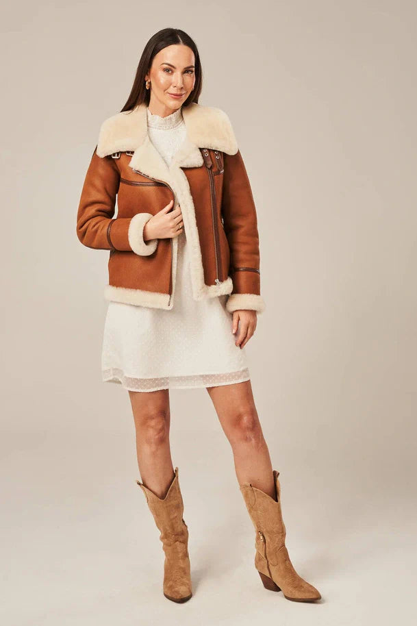 Woman wearing a brown leather jacket with white fur trim and matching boots on a beige background