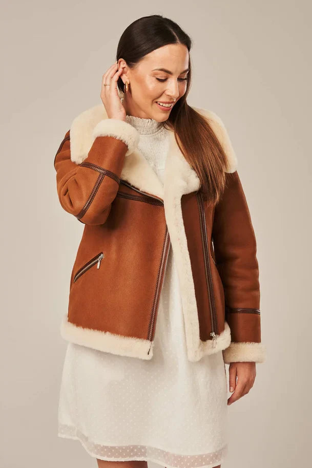 Woman wearing a brown shearling jacket with white fur trim on a beige background