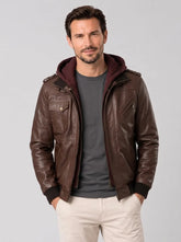 Male model wearing a dark brown leather bomber jacket with a burgundy hood, shoulder epaulets, chest detailing and ribbed cuffs.