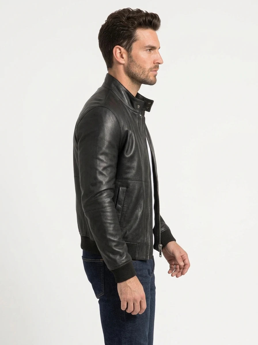 Male model wearing a black leather bomber jacket over a white T-shirt, showing the stand-up collar, front zipper and ribbed cuffs.