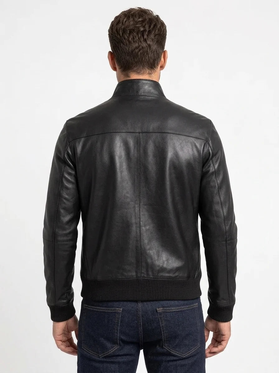 Back view of a black leather bomber jacket on a male model, showing the shoulder yoke, center seam and ribbed waistband.