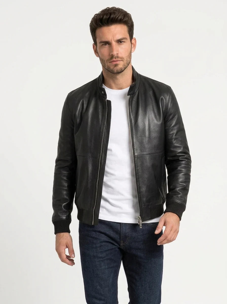 Male model wearing a black leather bomber jacket over a white T-shirt, showing the stand-up collar, front zipper and ribbed cuffs.