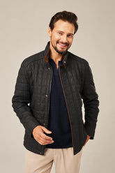 Man wearing a dark quilted jacket over a navy shirt with beige pants on a plain background