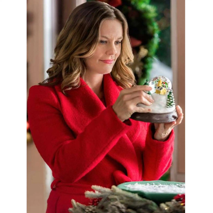 Woman in a red coat holding a small decorative item with a Christmas theme.