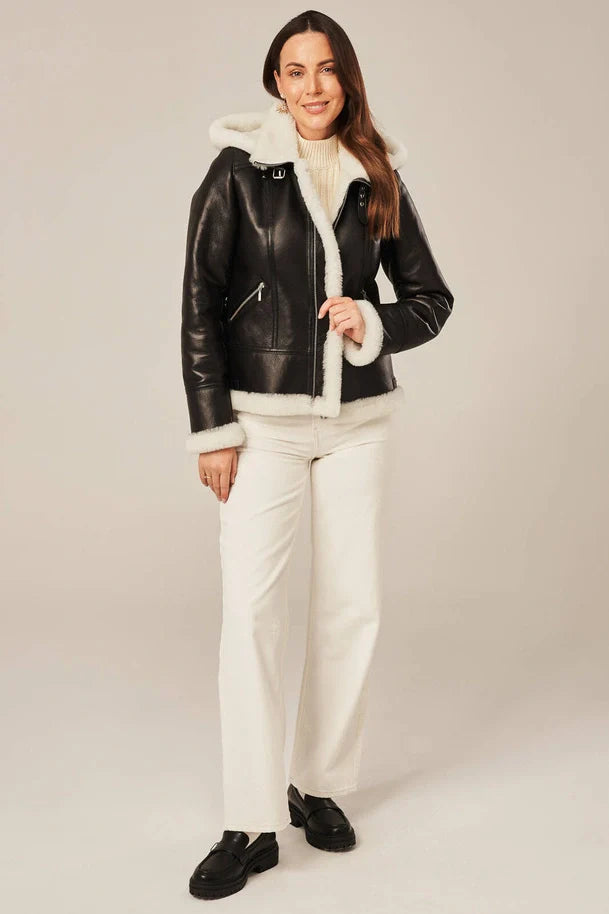 Woman wearing a black leather jacket with white fur lining on a plain background