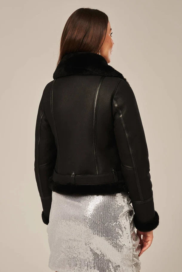 Person wearing a black leather jacket with fur collar on a beige background