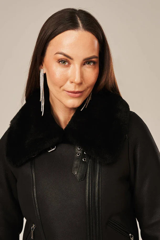 Woman wearing a black coat with a fur collar against a neutral background