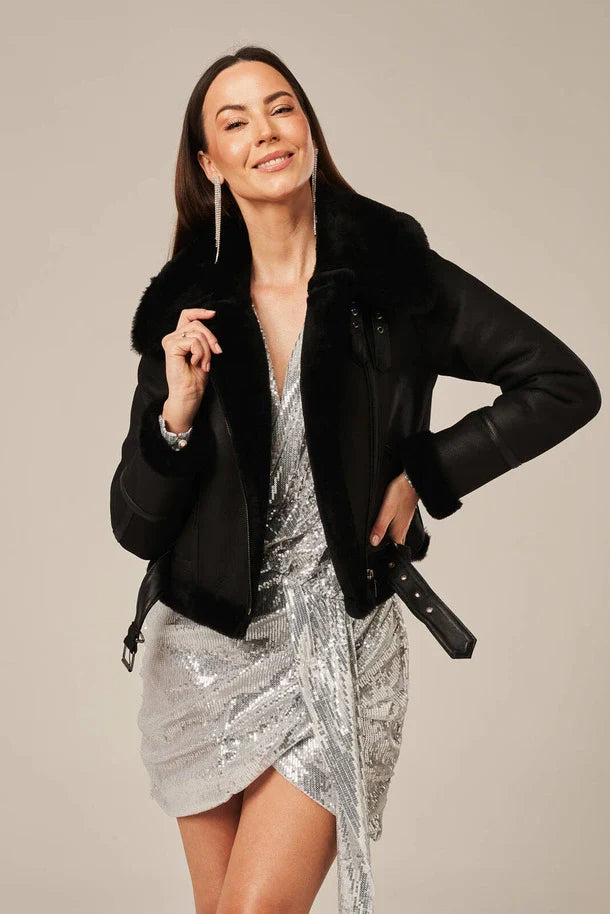 Woman wearing a black coat over a silver sequin dress on a neutral background
