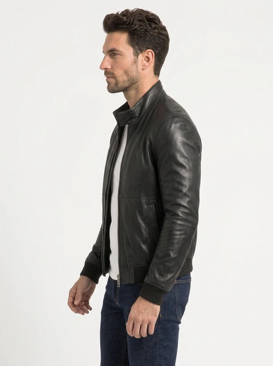 Male model wearing a black leather bomber jacket over a white T-shirt, showing the stand-up collar, front zipper and ribbed cuffs.