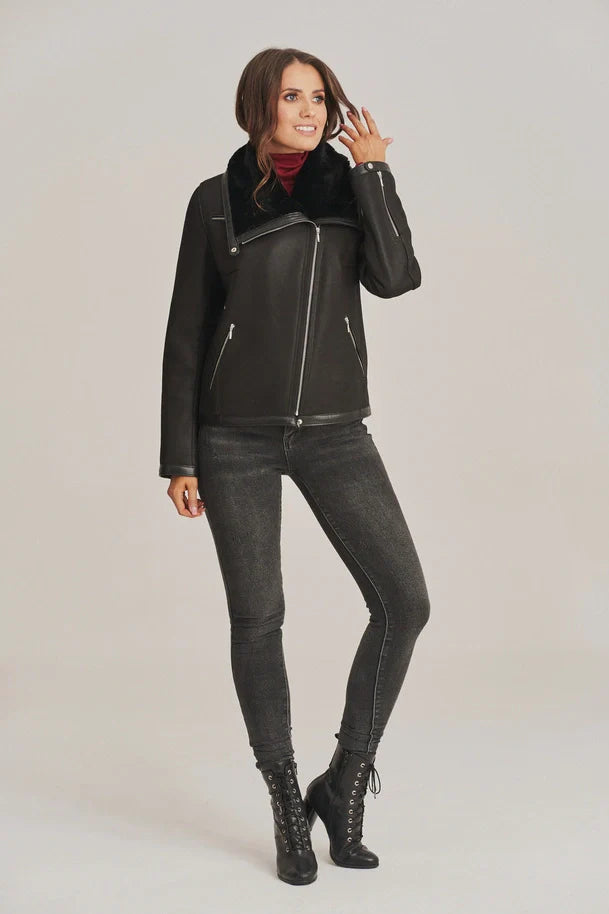 Woman wearing a black leather jacket, black jeans, and black boots on a light gray background