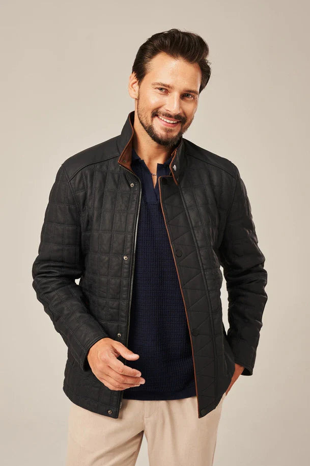 Man wearing a dark quilted jacket over a navy shirt with beige pants on a plain background