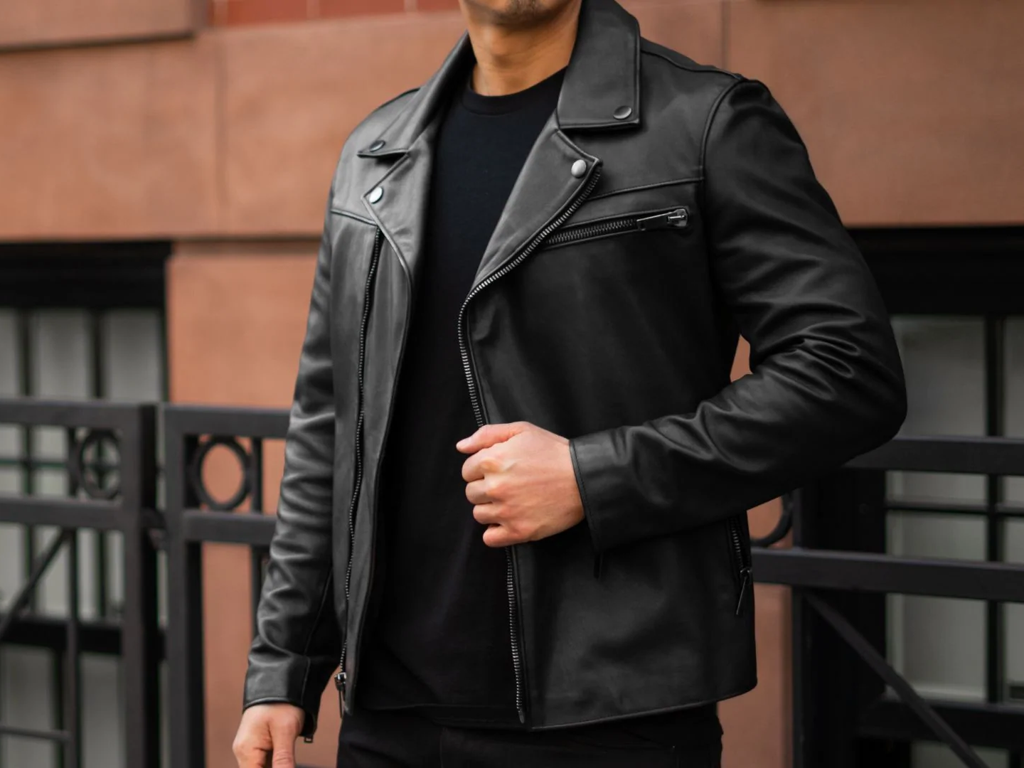 Person wearing a black leather jacket in front of a brick wall.