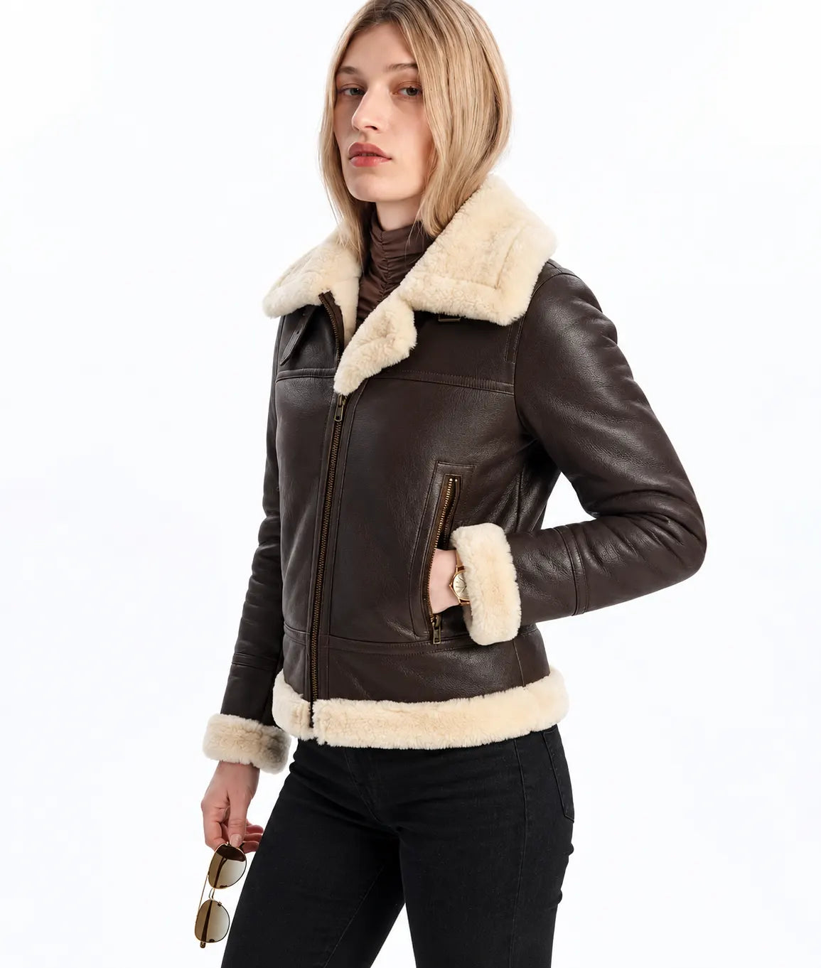 A woman wearing a dark brown leather aviator-style jacket with thick cream shearling lining on the collar, cuffs, and hem, paired with black pants against a plain white background.